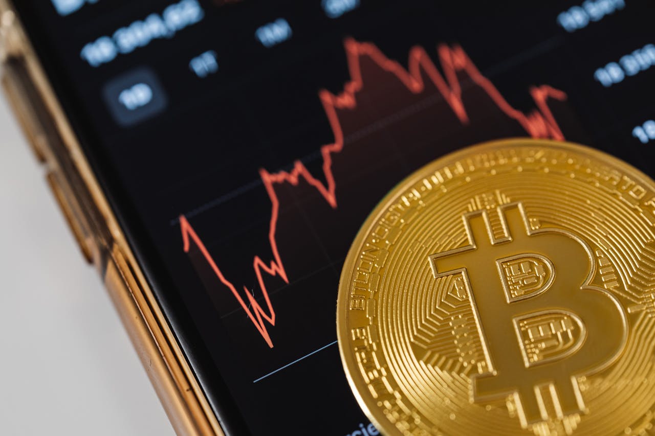 Services A gold Bitcoin coin on a smartphone displaying a fluctuating stock market chart.